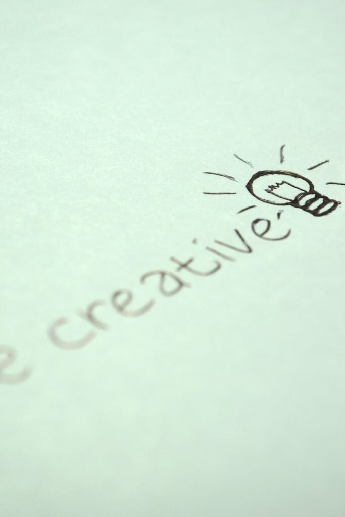 Close-up of handwritten 'Be creative' with a light bulb sketch on paper.